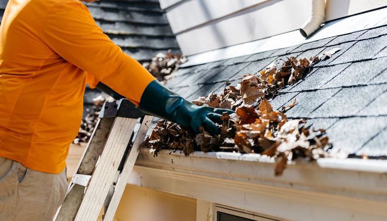 A man removing leaf from roof gutters during cleaning in Portland, Oregon