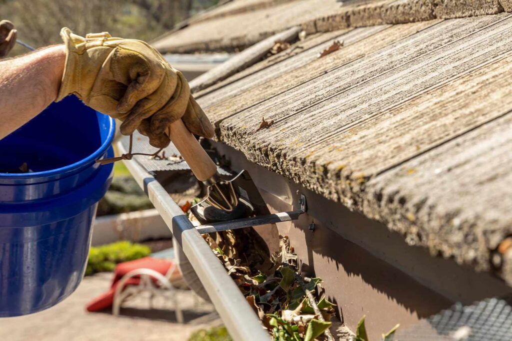 a gutter cleaner removing debris from gutters using a gutter scoop and bucket