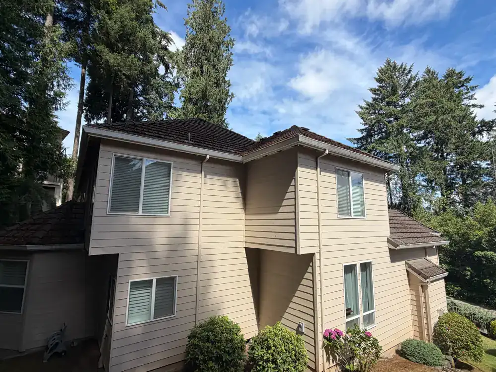 Two-story home in Beaverton, Oregon with a clean roof and gutters under tall fir trees