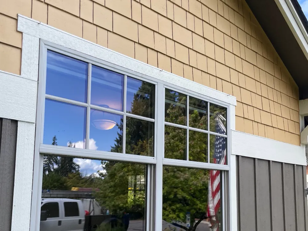Clean exterior windows on a shingle-sided house, clear enough to reflect the trees and sky