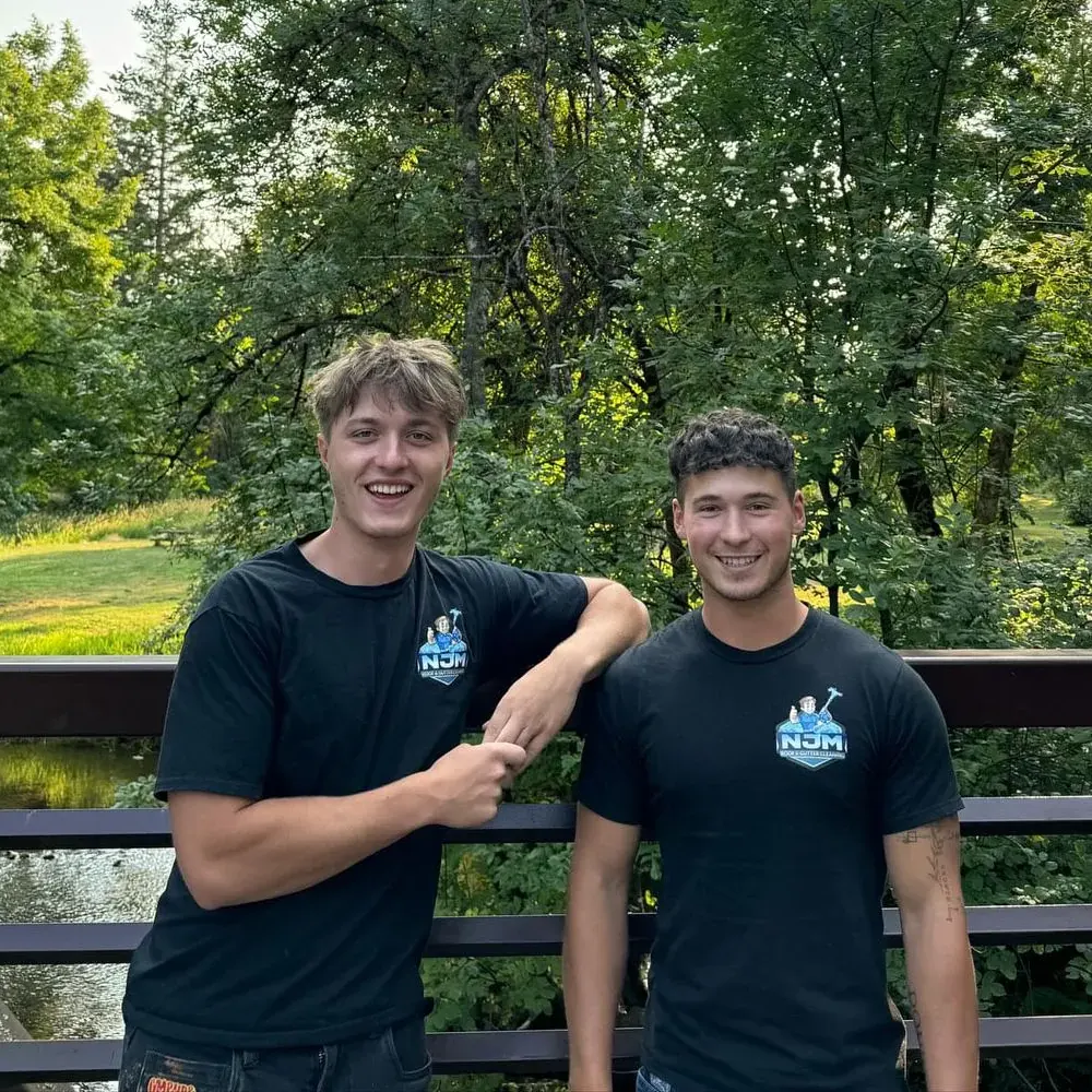 Two members of the NJM Roof & Gutter Cleaning team in black NJM logo shirts, standing on a footbridge